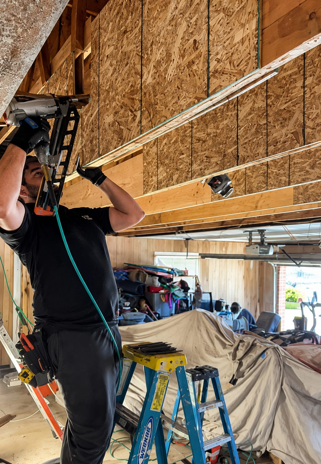 A crew member nailing new material to the ceiling framing from a ladder, Great Falls, VA